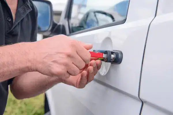 Experienced and Qualified Technicians 2 - SMC Towing Group Person using a tool to pry open the handle of a white car door outdoors.