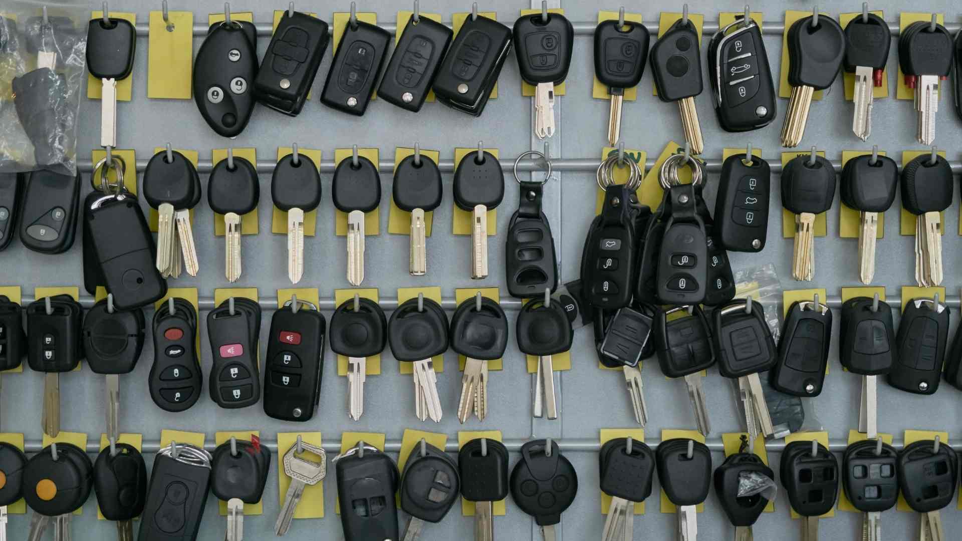 Many car keys and remotes hang on a metal display rack with yellow tags and hooks, arranged in rows.