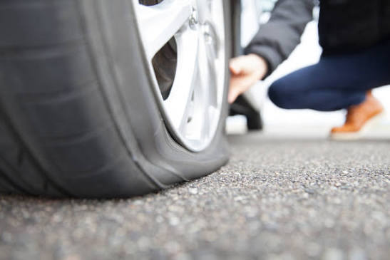 Can You Drive With a Flat Tire Risks Distance What to Do - SMC Towing Group Close-up of a car tire on asphalt as a person crouches beside the vehicle, inspecting the wheel.