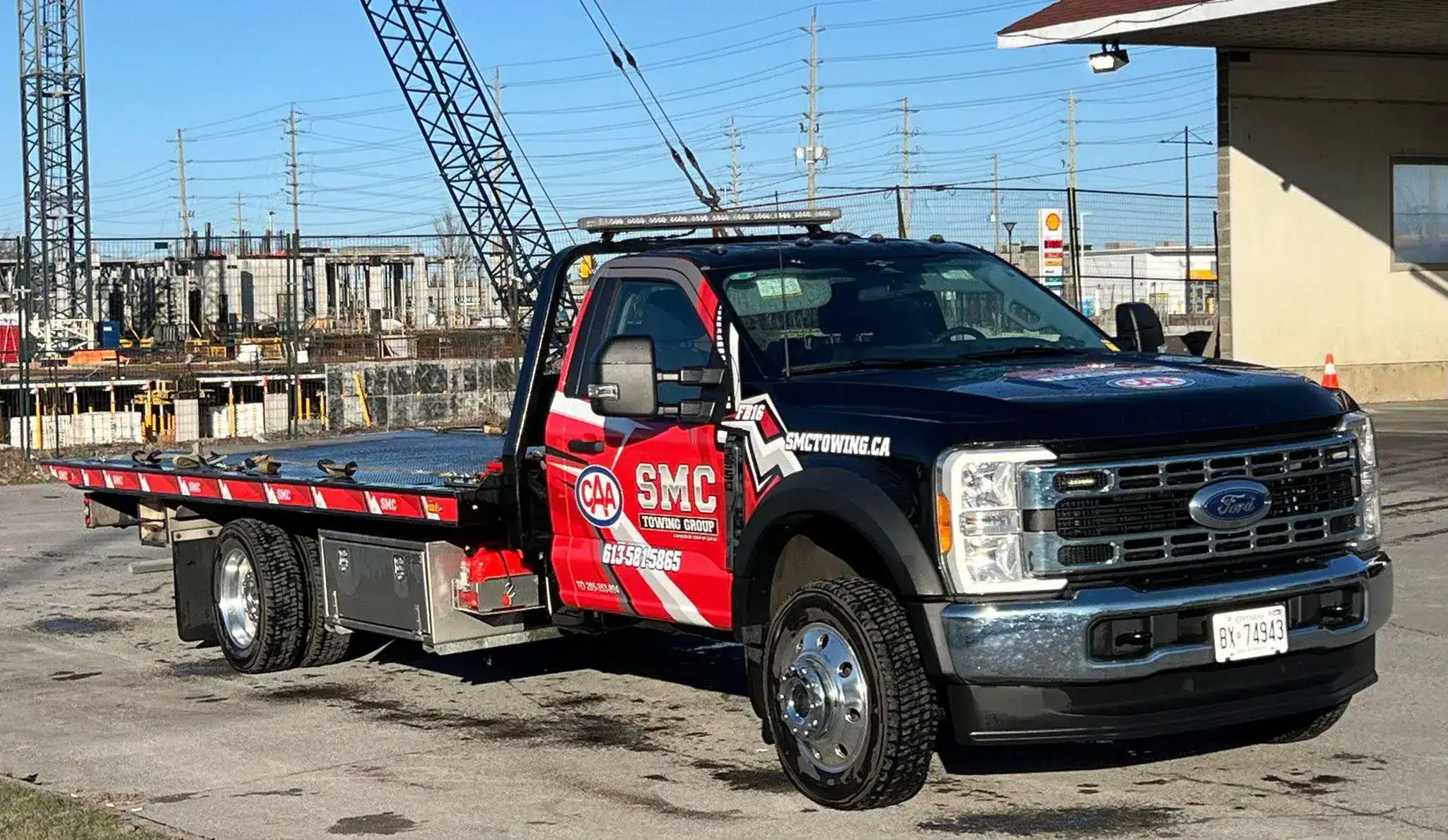 Tow truck with red and black livery, flatbed extended, parked near a construction site.